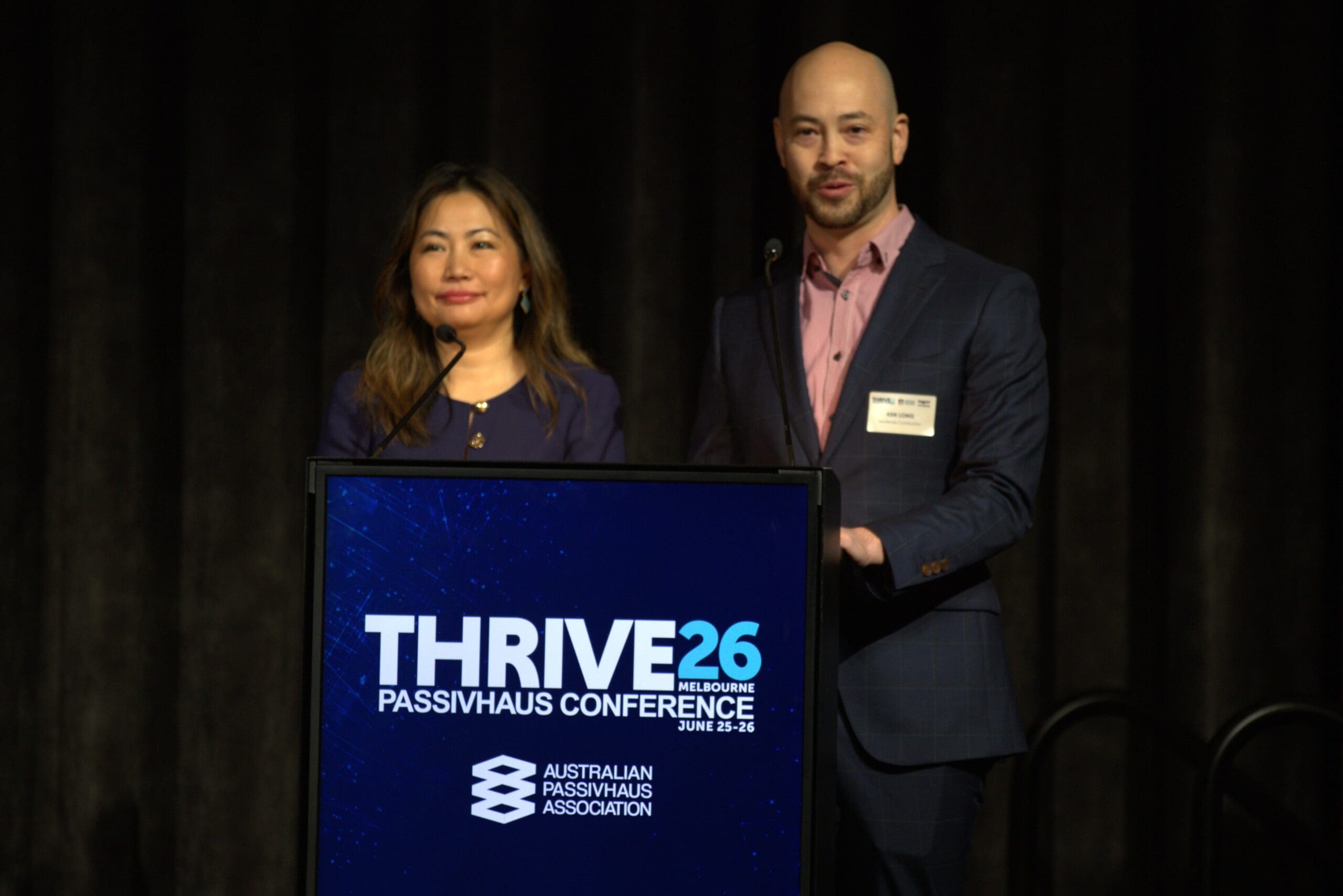 woman and man stand in front of a podium with "thrive26" logo
